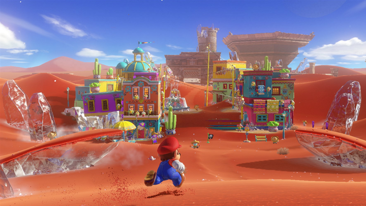 Super Mario Odyssey screenshot showing Mario running across a red desert landscape toward a small town in the distance.